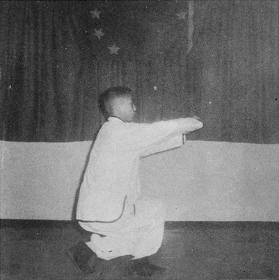 Posture 8 : pas de l’anneau à droite, avant-bras droit roulé de côté, poing gauche poussant au poignet — photographie de l’édition de 1972