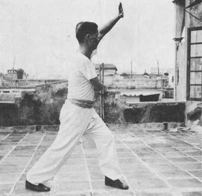 Posture 20a : le pied droit reculé, paume gauche haute, main droite aux côtes — photographie de l’édition de 1971