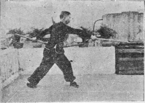 Posture 28, position de passage A (planche 28a) : le bâton soulevé de terre, la main droite ressaisissant l&rsquo;autre extrémité