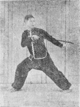 Posture 26, position de passage (planche 26a) : le pied droit ouvert vers l&rsquo;est, le sabre et la main crochue gauche légèrement écartés, le regard vers l&rsquo;arrière-ouest