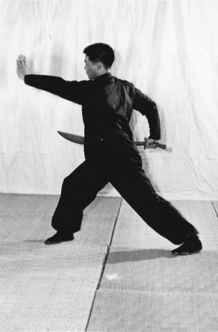 Posture 18 (planche 18) : relevé après la roulade, la posture de l&rsquo;ascension à droite, le sabre tiré au-dessus de l&rsquo;épaule droite puis ressorti par l&rsquo;épaule gauche