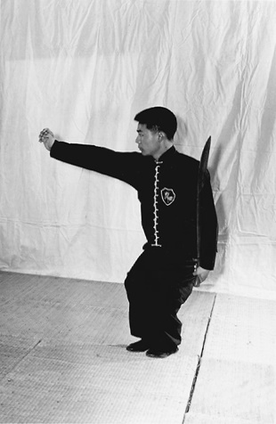 Posture 20, position de passage A (planche 20a) : les jambes fléchies, la main droite passant près de l&rsquo;épaule gauche et s&rsquo;étendant vers la droite comme pour saisir une gourde