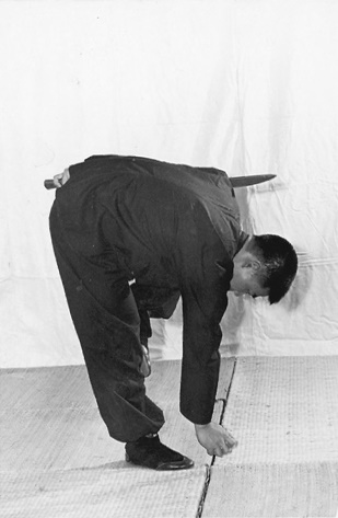 Posture 23, position de passage C (planche 23c) : la flexion profonde vers le sol, la jambe d&rsquo;appui tendue, la main descendant vers le sol