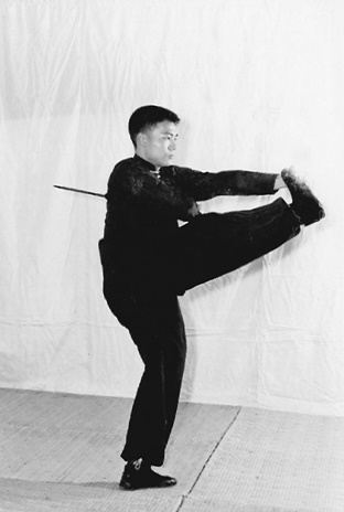 Posture 6 (planche 6) : en pleine rotation du coup de pied tourbillon vers l&rsquo;est, le sabre ramené contre la taille gauche